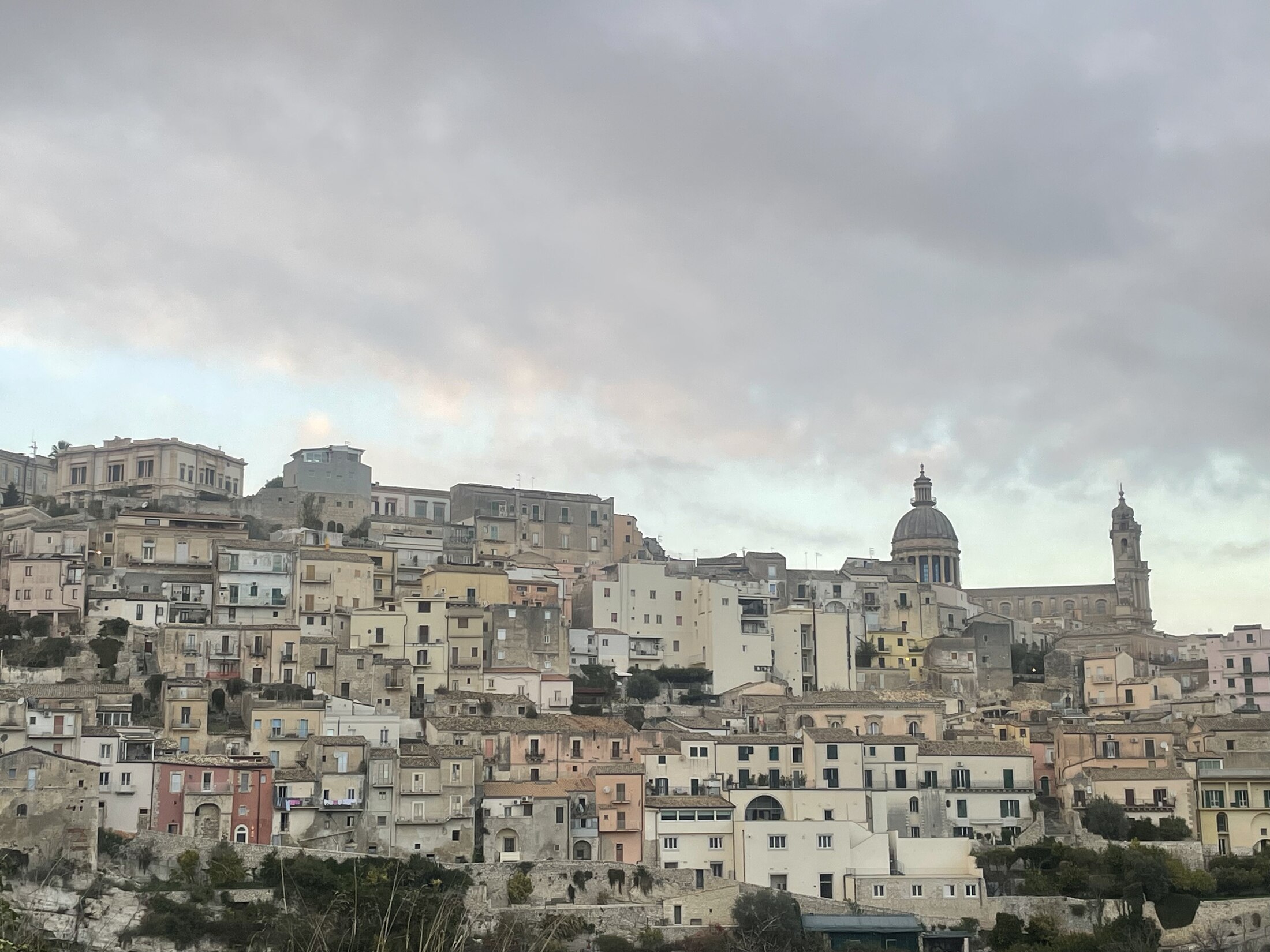 A Sicilian hill town rising beneath a cloudy sky