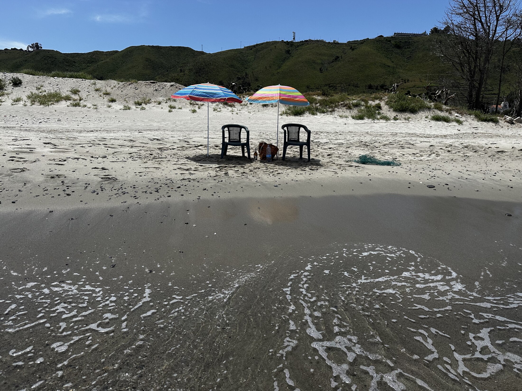 Two colorful umbrellas and chairs at the water's edge